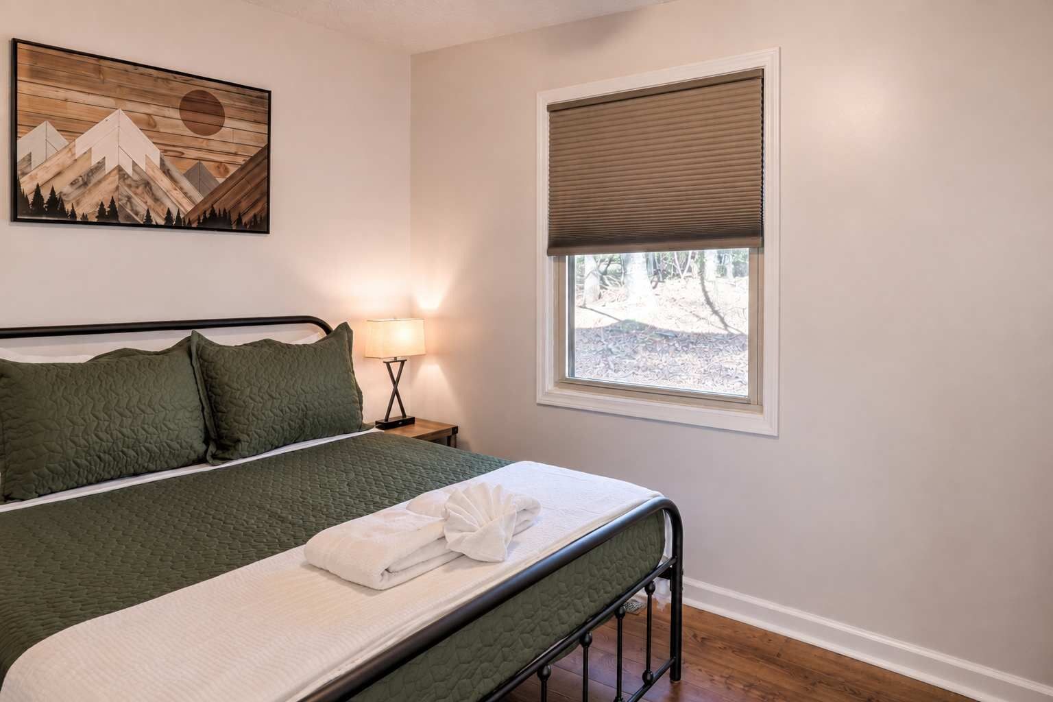 Un dormitorio con cama, lámpara de noche, ventana con persiana y un cuadro en la pared.