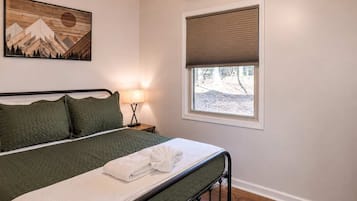 Un dormitorio con cama, lámpara de noche, ventana con persiana y un cuadro en la pared.