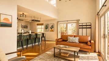 A spacious living room with a brown leather sofa, a coffee table, and a dining area with a bar.