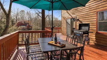 Una terraza al aire libre con una mesa, sillas, una parrilla y un gran paraguas.