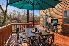 Una terraza al aire libre con una mesa, sillas, una parrilla y un gran paraguas.