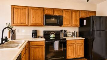 Una cocina con armarios de madera, un microondas negro, un refrigerador negro, una estufa y un ventilador de techo.