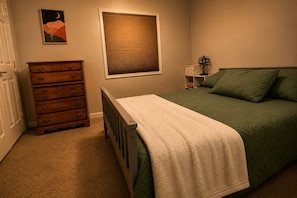 Ein Schlafzimmer mit Bett, Kommode, Fenster und einem Kunstwerk an der Wand.