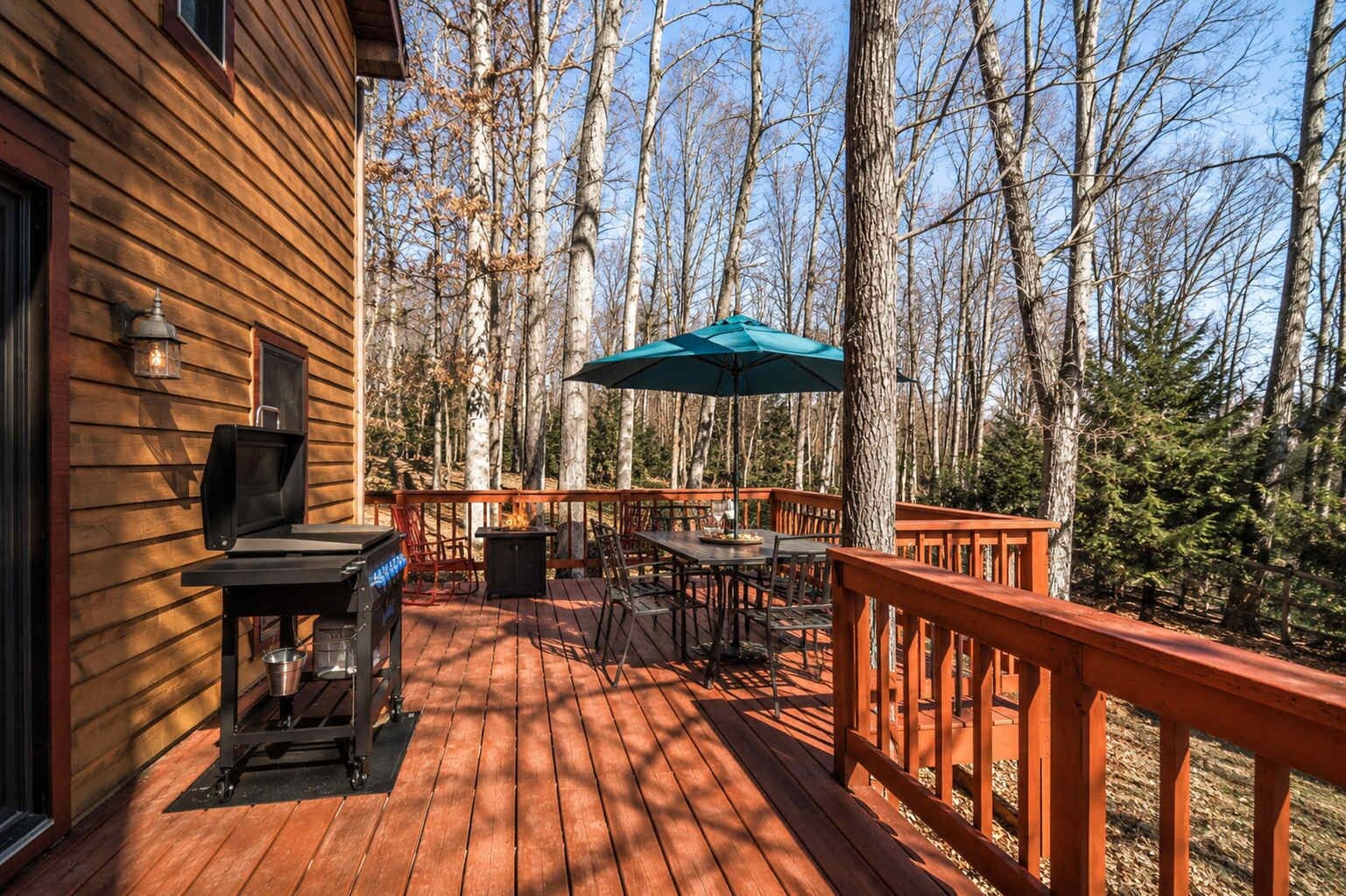 A wooden deck with a barbecue grill, outdoor table and chairs, and a large umbrella.