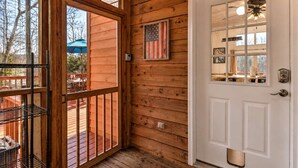 Una baita di legno con una porta bianca, un balcone con ringhiera metallica e una bandiera americana alla parete.