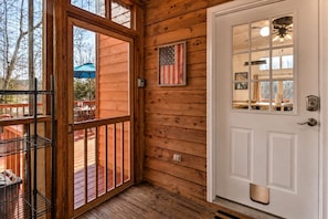 Eine Holzhütte mit einer weißen Tür, einem Balkon mit Metallgeländer und einer amerikanischen Flagge an der Wand.