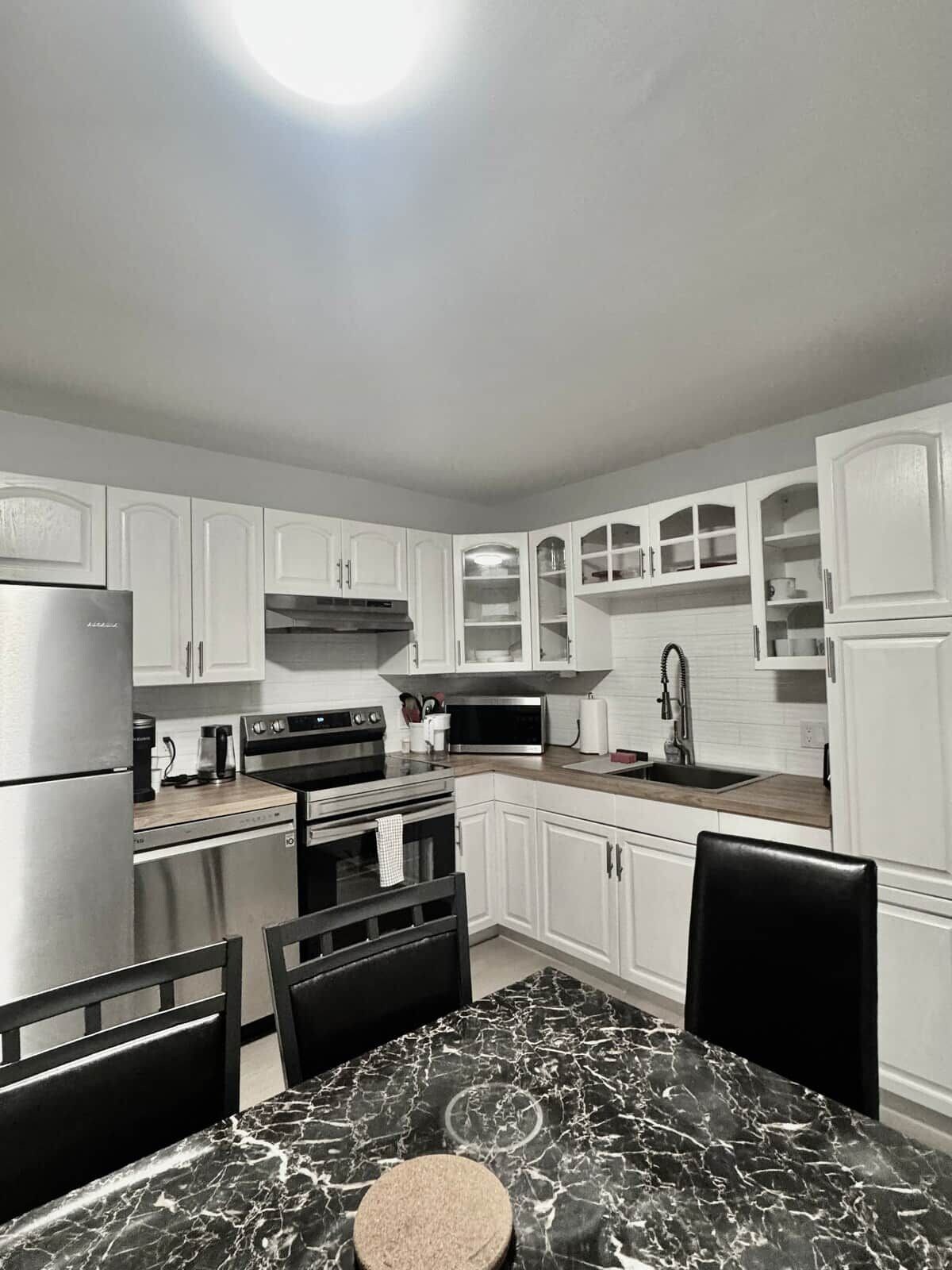 A modern kitchen with white cabinetry, stainless steel appliances, and a marble countertop.
