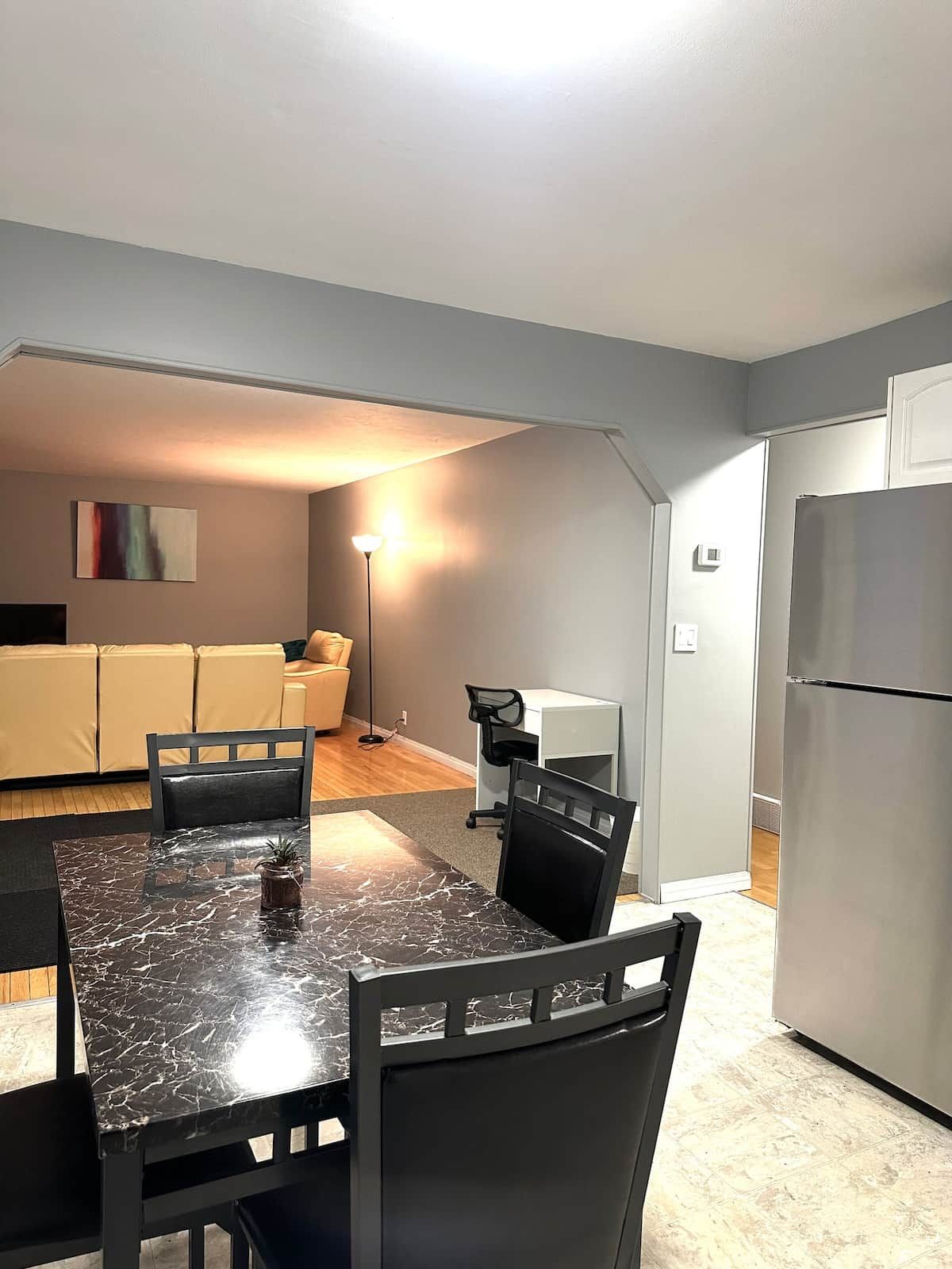 A compact living space with a dining table, chairs, a sofa, a floor lamp, and a refrigerator.