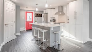 A modern kitchen with a central island, bar stools, and white cabinetry. - Warm & Modern Home in Yellowknife | Sleeps 5 (Yellowknife)