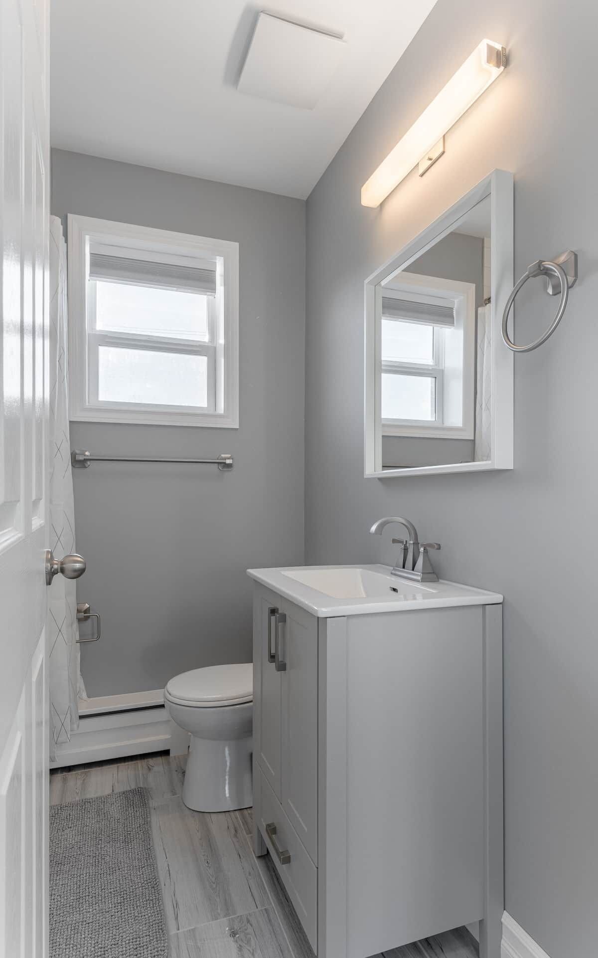 A bathroom with a toilet, a sink, a mirror, and a window.