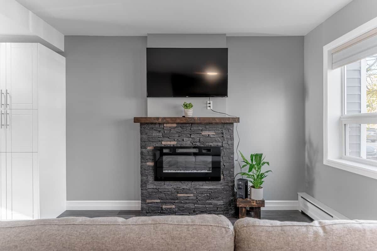 A living room with a stone fireplace, a mounted TV, and a window.