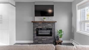 A living room with a stone fireplace, a mounted TV, and a window. - Warm & Modern Home in Yellowknife | Sleeps 5 (Yellowknife)