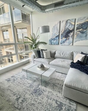 A modern living room with a grey sofa, a coffee table, and a large window. - Luxury 1 Bedroom Loft in Jersey City (Jersey City)