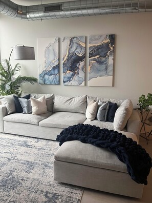 Ein Wohnzimmer mit grauem Sofa, einer dunklen Decke und abstrakter Kunst an der Wand.