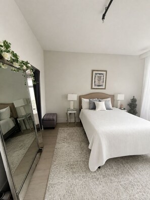 A hotel room with a large bed, bedside tables, a mirror, a framed picture on the wall, and a small potted plant. - Luxury 1 Bedroom Loft in Jersey City (Jersey City)