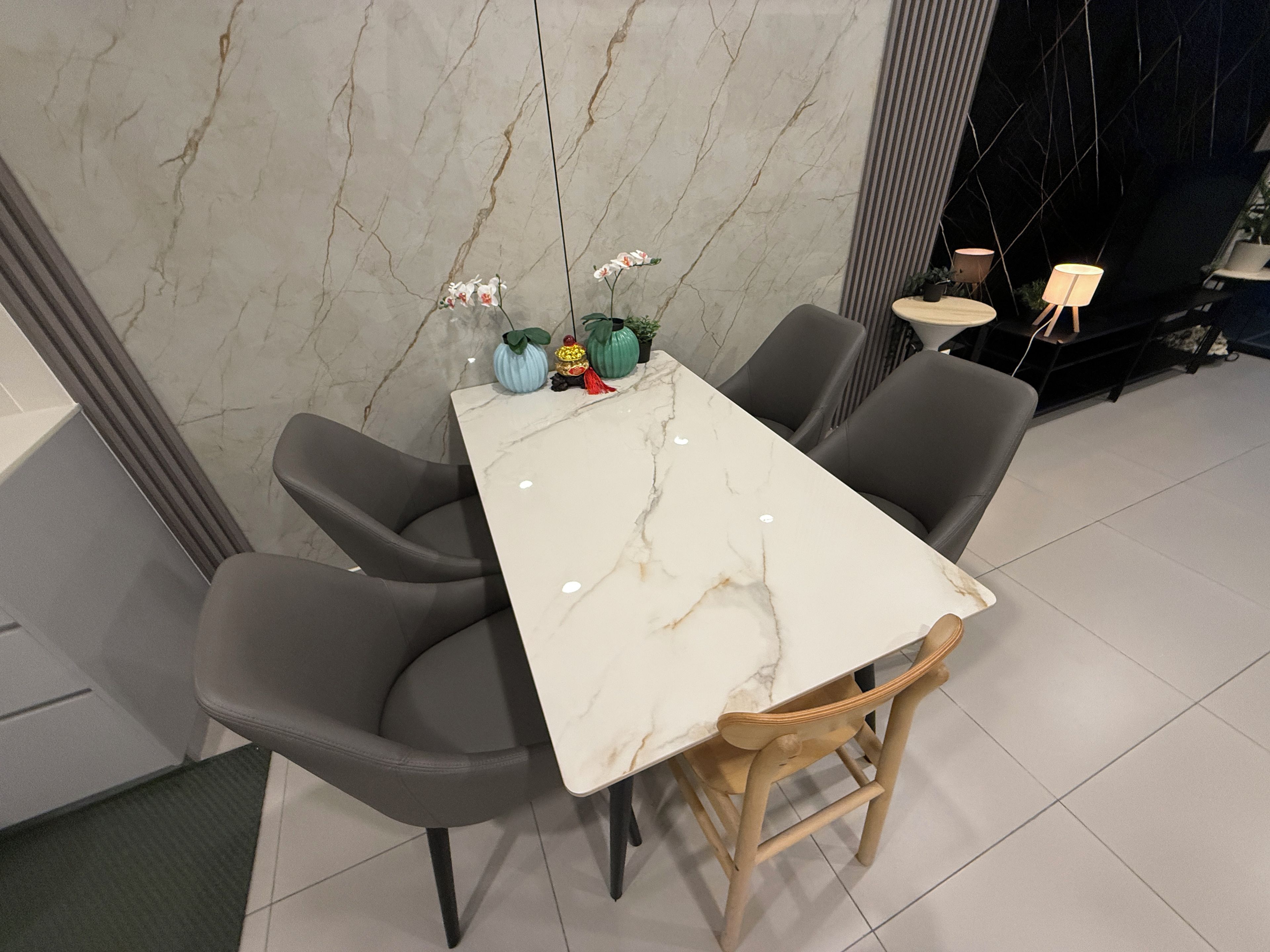 A dining area with a marble table, grey chairs, and small potted plants.