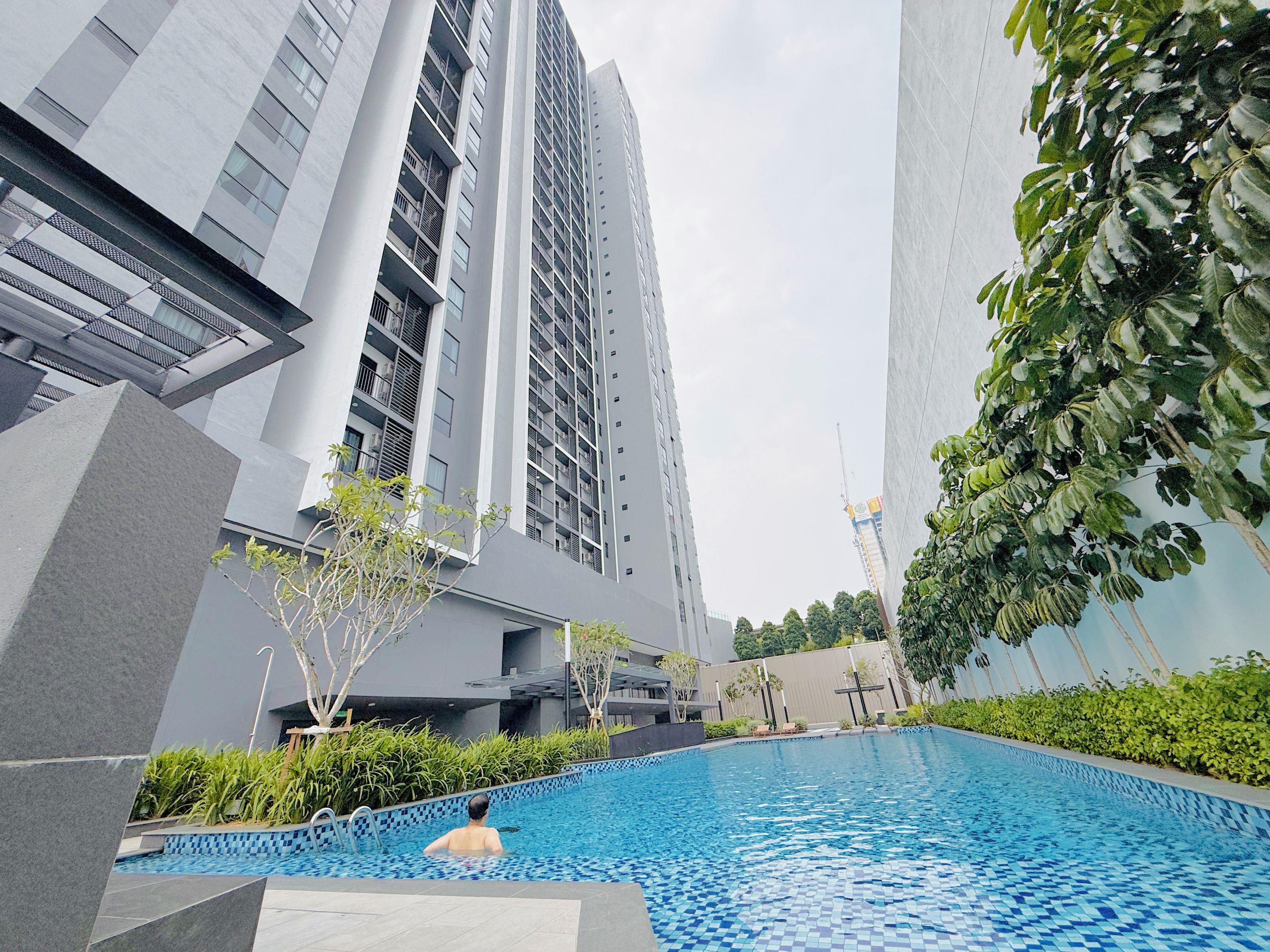 A modern building with a swimming pool, surrounded by greenery and other structures.