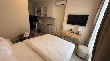A hotel room with a bed, a desk with a lamp, a TV, and a kitchenette area.