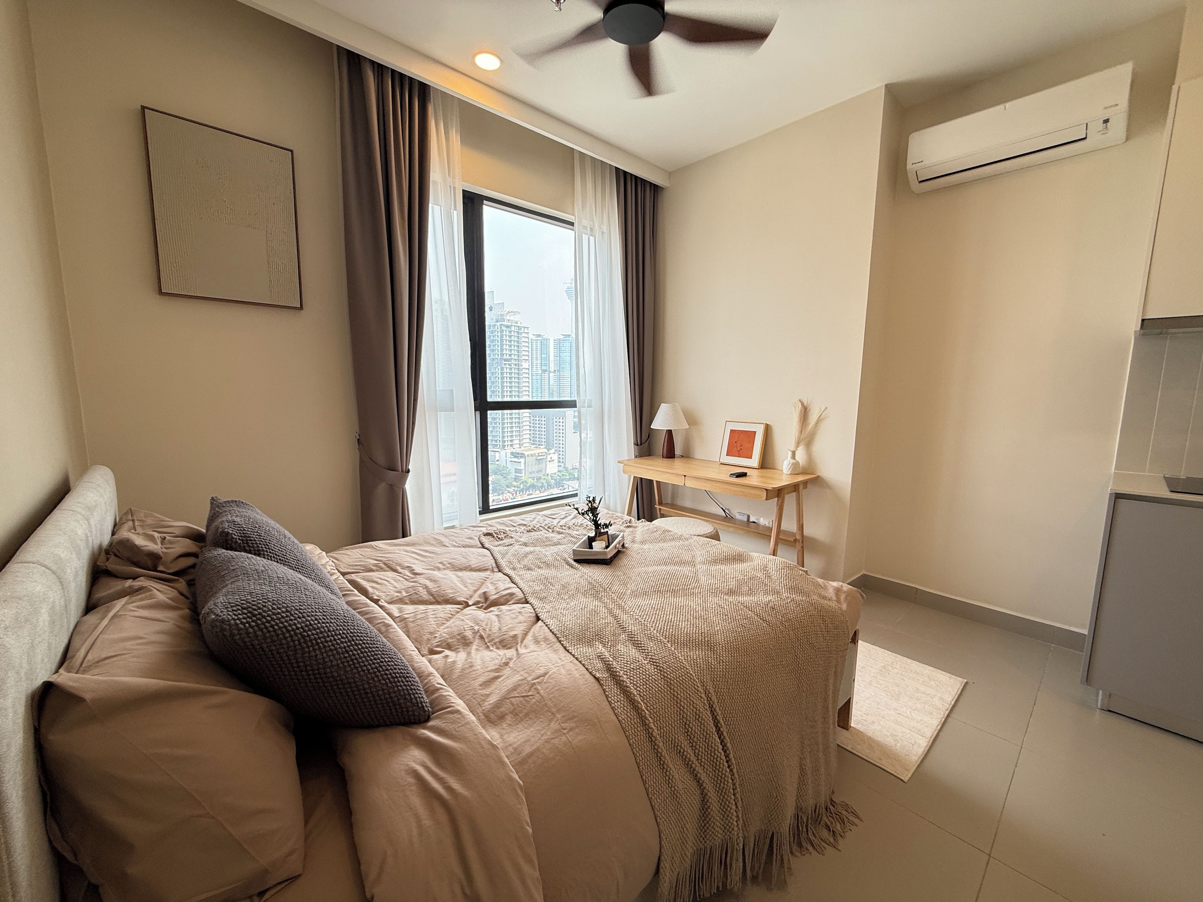 A bedroom with a bed, a desk, a window with curtains, and an air conditioning unit.
