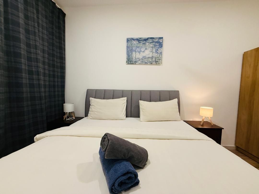 A hotel room with a bed, two pillows, a nightstand with a lamp, a painting on the wall, and a wardrobe.