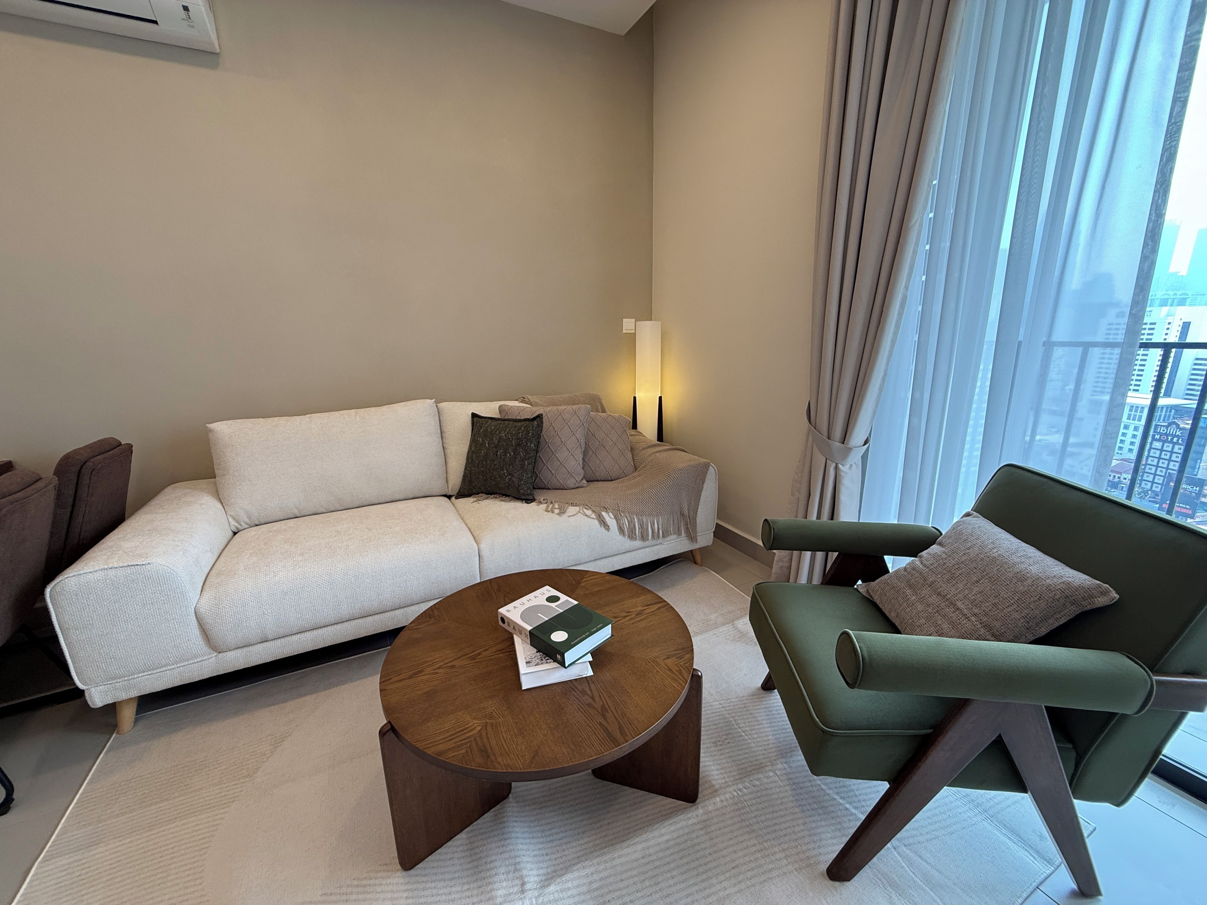 A modern living room with a sofa, a green armchair, a coffee table, and a view of the city through large windows.