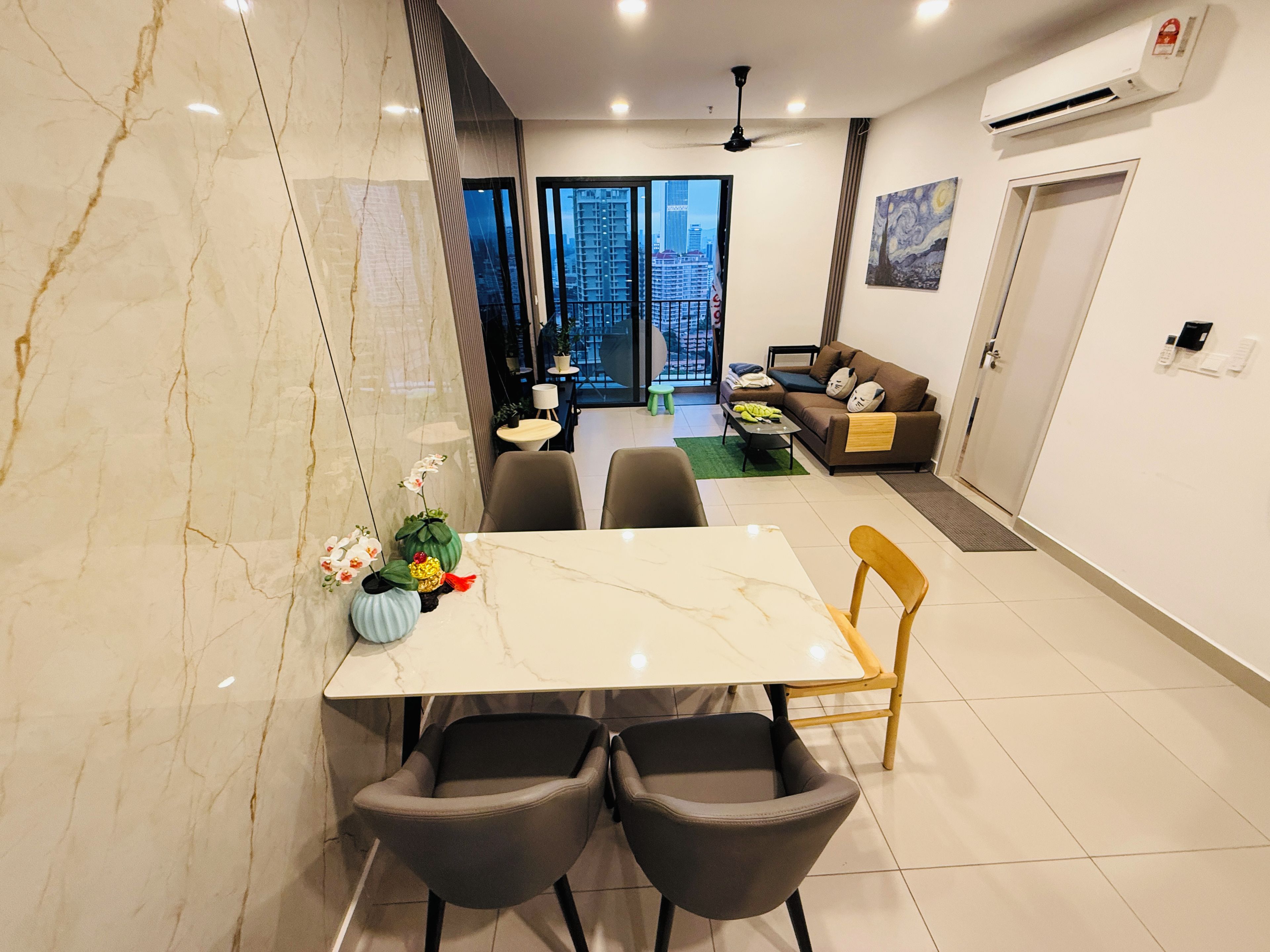 A modern living room with a sofa, a dining table with chairs, a view of the city through large windows, and an air conditioning unit on the wall.