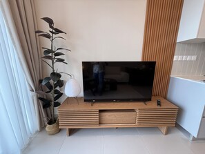 A flat-screen TV on a wooden TV stand with a plant beside it. - SWNK Houze LaLaport BBCC by HomeHorizon (Kuala Lumpur)