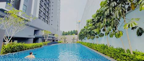 A swimming pool with a tiled edge, surrounded by greenery and modern buildings.