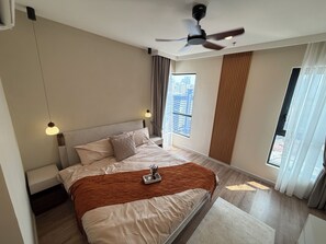A modern hotel room with a large bed, a ceiling fan, a window with curtains, and a city view. - SWNK Houze LaLaport BBCC by HomeHorizon (Kuala Lumpur)