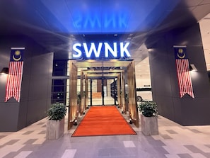 The entrance to a hotel with a red carpet, a sign reading 'SWNK', and Malaysian flags on either side. - SWNK Houze LaLaport BBCC by HomeHorizon (Kuala Lumpur)