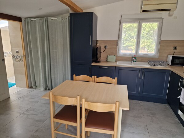 Cuina amb taula de menjador, cadires, microones, torradora i finestra amb vista a vegetació.