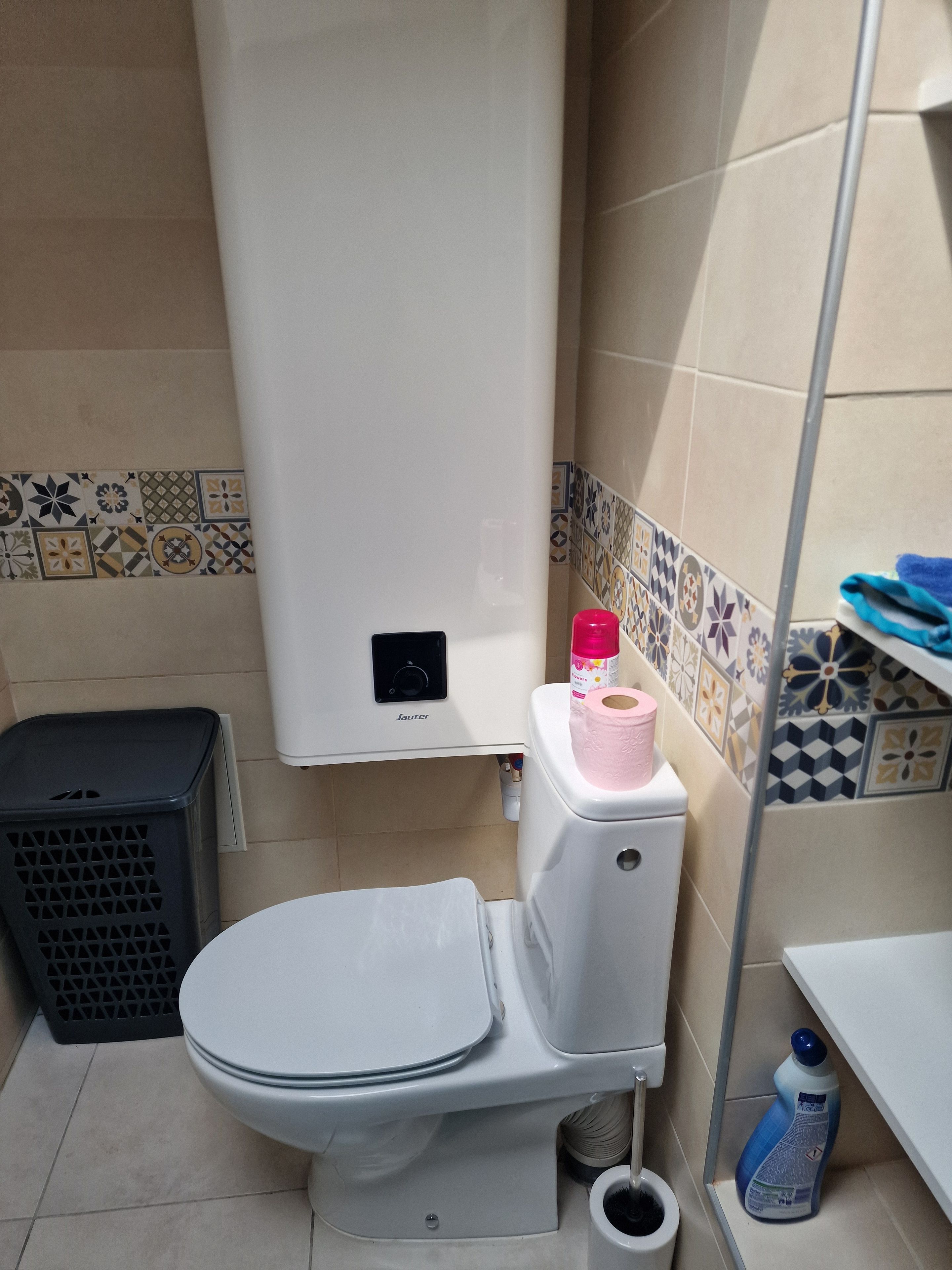 Une salle de bain équipée de toilettes, d’une poubelle, d’un porte-rouleau de papier toilette et d’un produit de nettoyage.