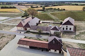 Ein Weingut mit mehreren Gebäuden, darunter ein großes Haus und einige kleinere Bauten, umgeben von Feldern und einer Straße.