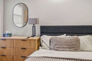 Een slaapkamer met een bed, een nachtkastje met een lamp, een spiegel en een houten kledingkast.