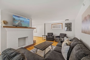 A living room with a fireplace, a sofa, a coffee table, and a television mounted above the fireplace.
