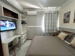 Ein Schlafzimmer mit einem Bett, einem Schreibtisch, einem Stuhl, einem Fernseher, einem Kleiderschrank und einem Fenster mit Vorhängen.