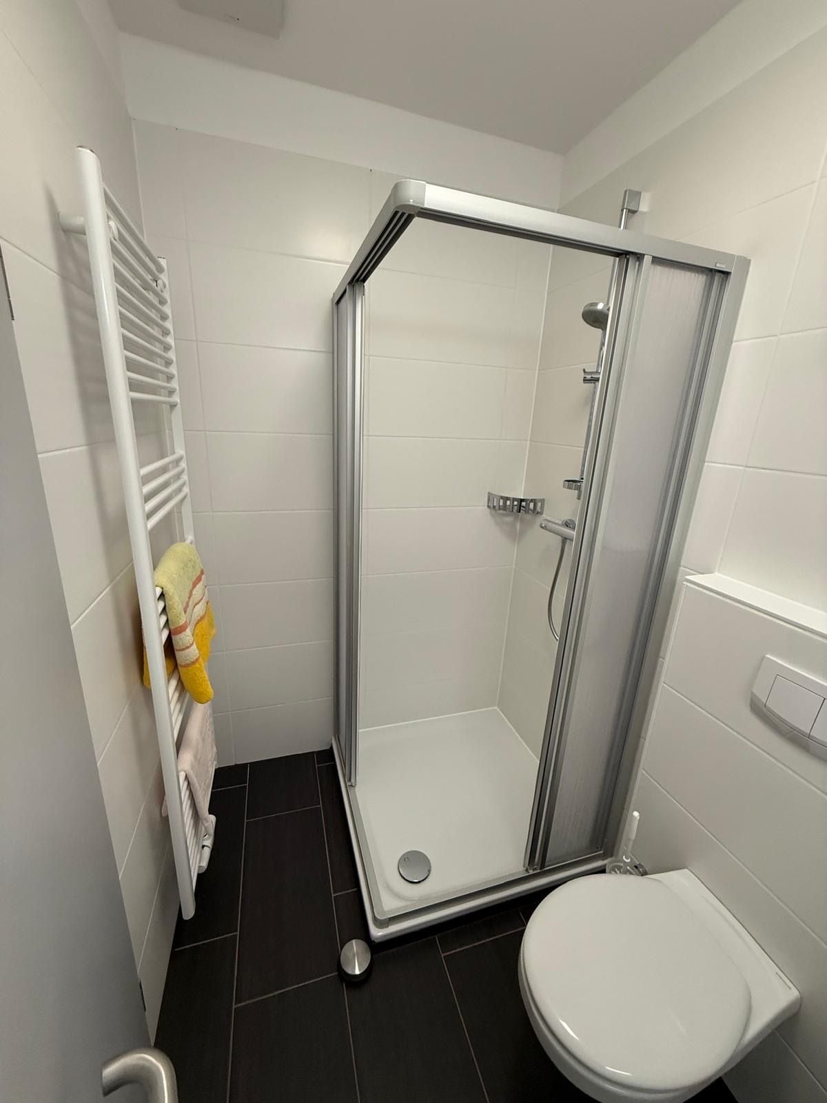 Un baño moderno con ducha envuelta en vidrio, inodoro blanco y toallero con una toalla amarilla.