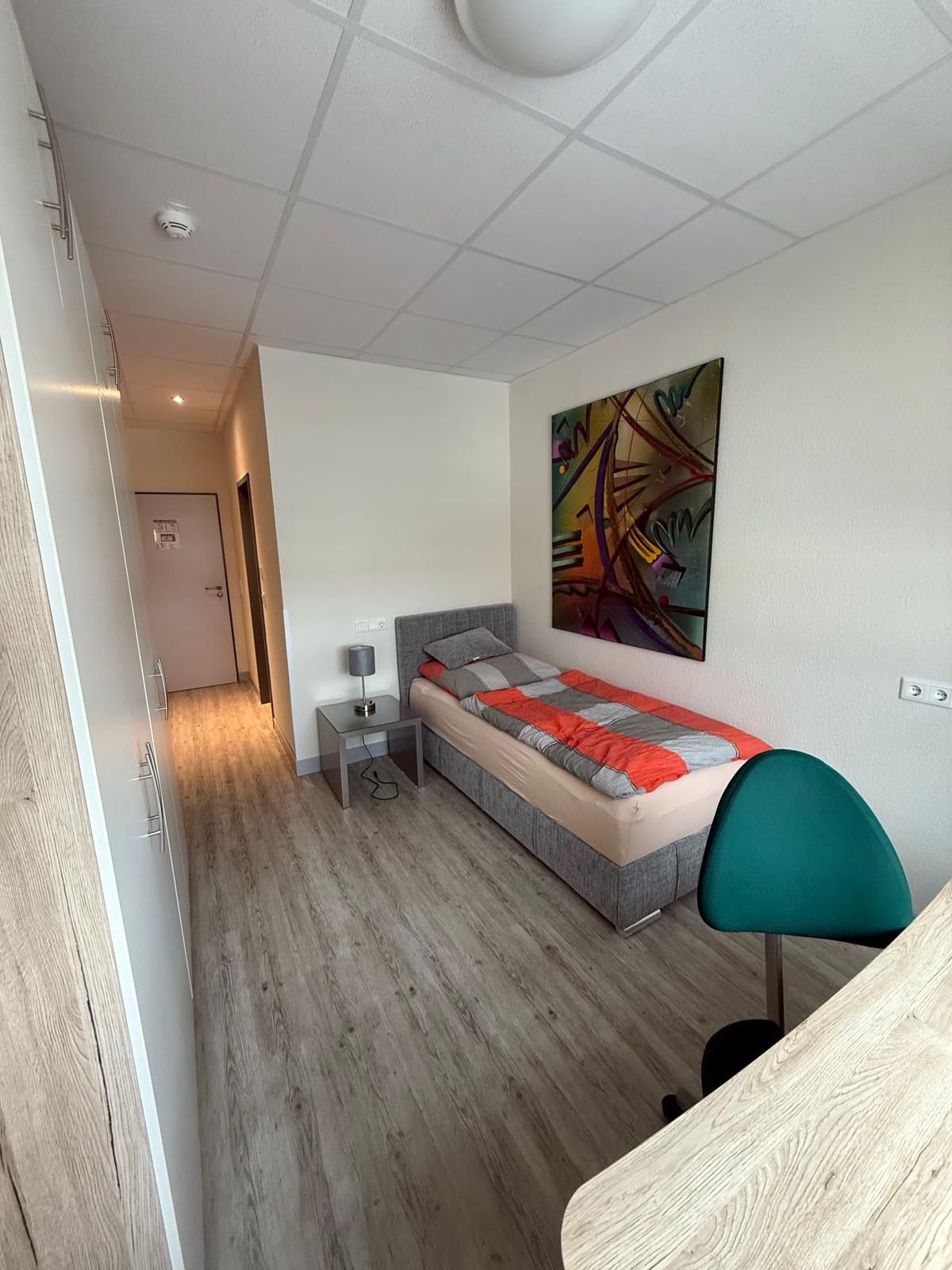 Une chambre à coucher avec un lit, une table de chevet, une lampe et un tableau abstrait aux couleurs vives accroché au mur.