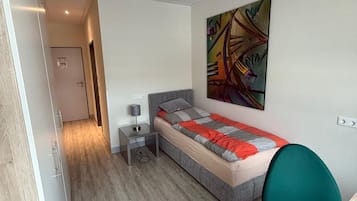 Ein Schlafzimmer mit Bett, Nachttisch, Lampe und einem farbenfrohen abstrakten Gemälde an der Wand.