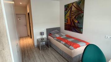 A modern bedroom with a bed, bedside table, lamp, and a colorful abstract painting on the wall.
