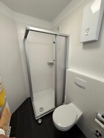 Un baño con ducha envuelta en vidrio, inodoro y toallero con toallas.