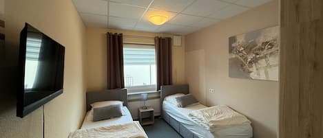 A hotel room with two beds, a TV, a desk, and a window with curtains.