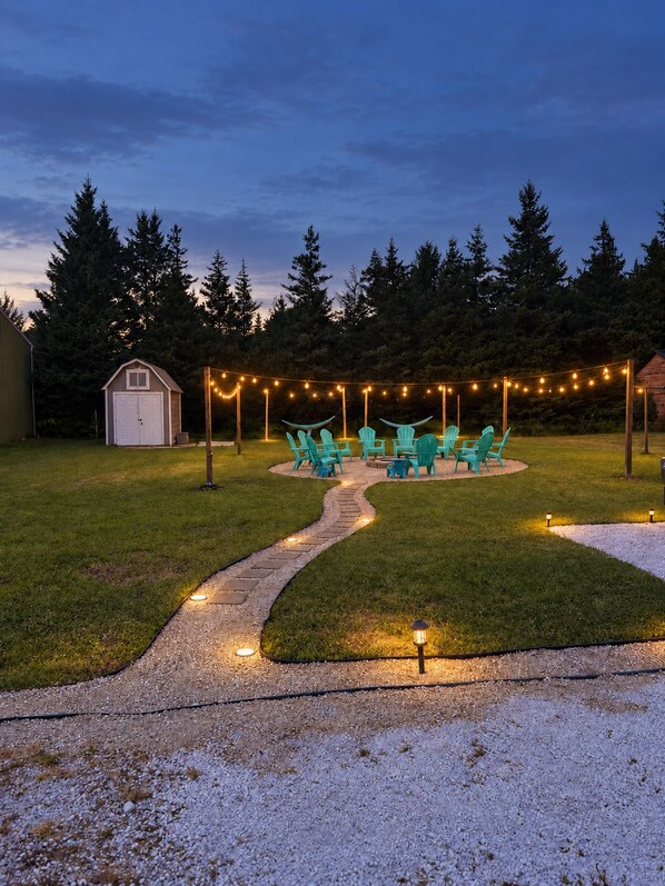 Ein Garten mit befestigtem Weg, einer Sitzgelegenheit mit Stühlen und Lichterketten.