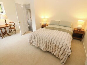 Un dormitorio con una cama, dos mesitas de noche con lámparas, una silla y una puerta que da a un baño.