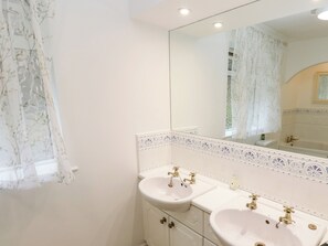 Un baño con dos lavamanos, un espejo y una ventana con cortinas florales.