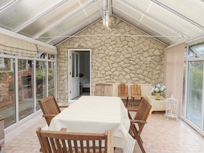 Un patio cubierto con pared de piedra, una mesa con sillas y vistas a través de puertas de cristal grandes.