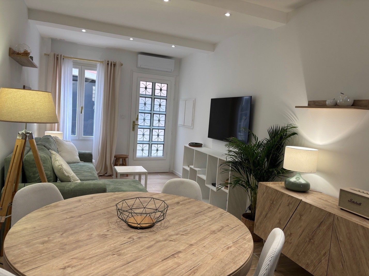 Un salon moderne avec une table ronde en bois, un canapé, un téléviseur et une plante.