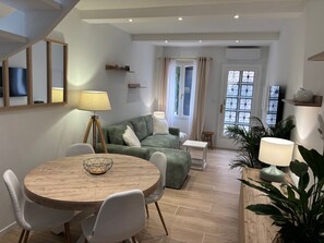 A modern living room with a round wooden table, a green sofa, and a small white side table. - L'Intramuros ★ A/C & Free Parking Pass in the Heart of the Ramparts (Aigues-Mortes)