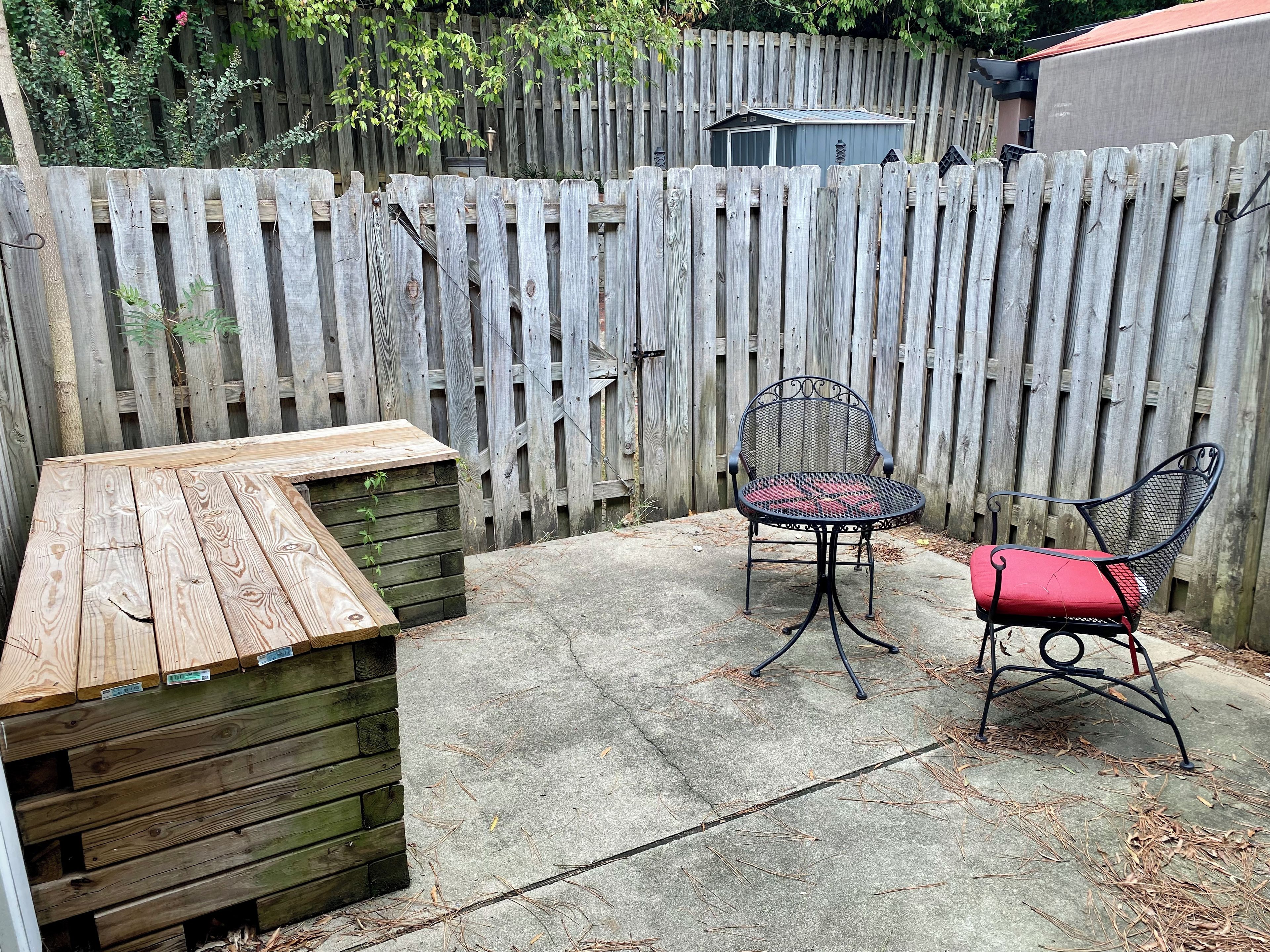 Un espace patio comprenant une table en bois et deux chaises, un banc en bois et une clôture en bois.
