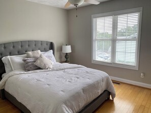 Quarto com cama, mesa de cabeceira, abajur e janela com persianas.